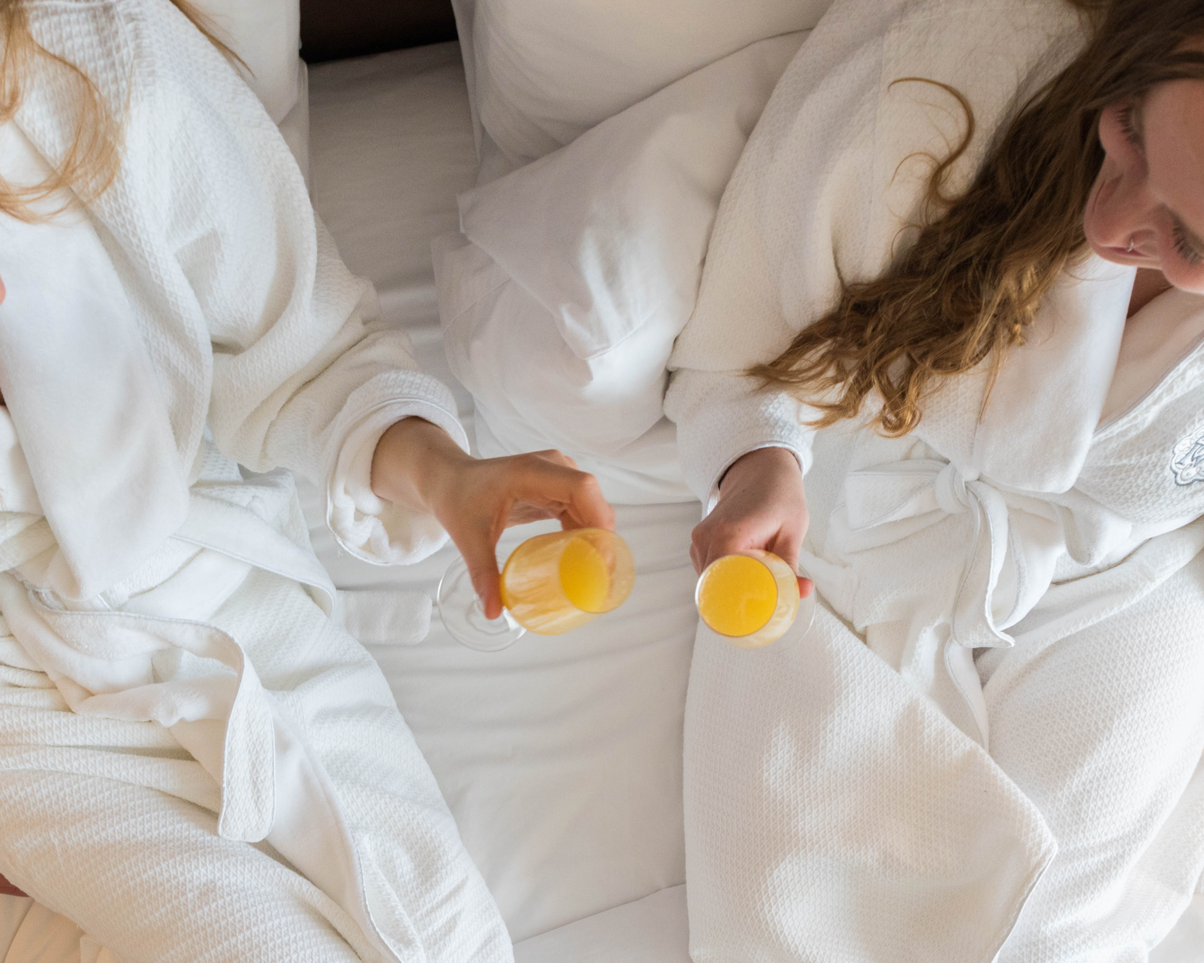 Two women cheers mimosas in bed at Magnolia Hotel & Spa