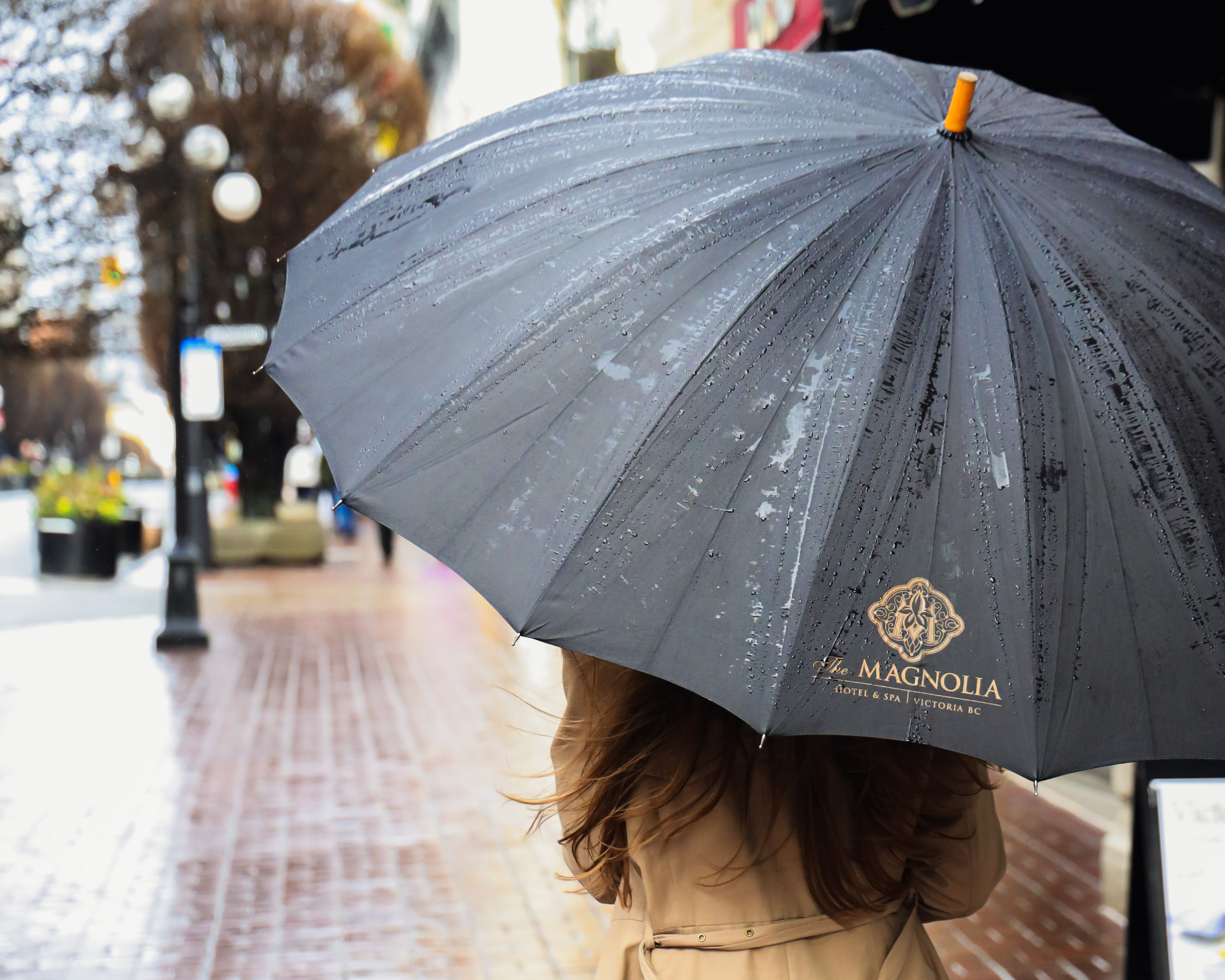 A woman walks on a rainy street with a Magnolia Hotel & Spa branded umbrella