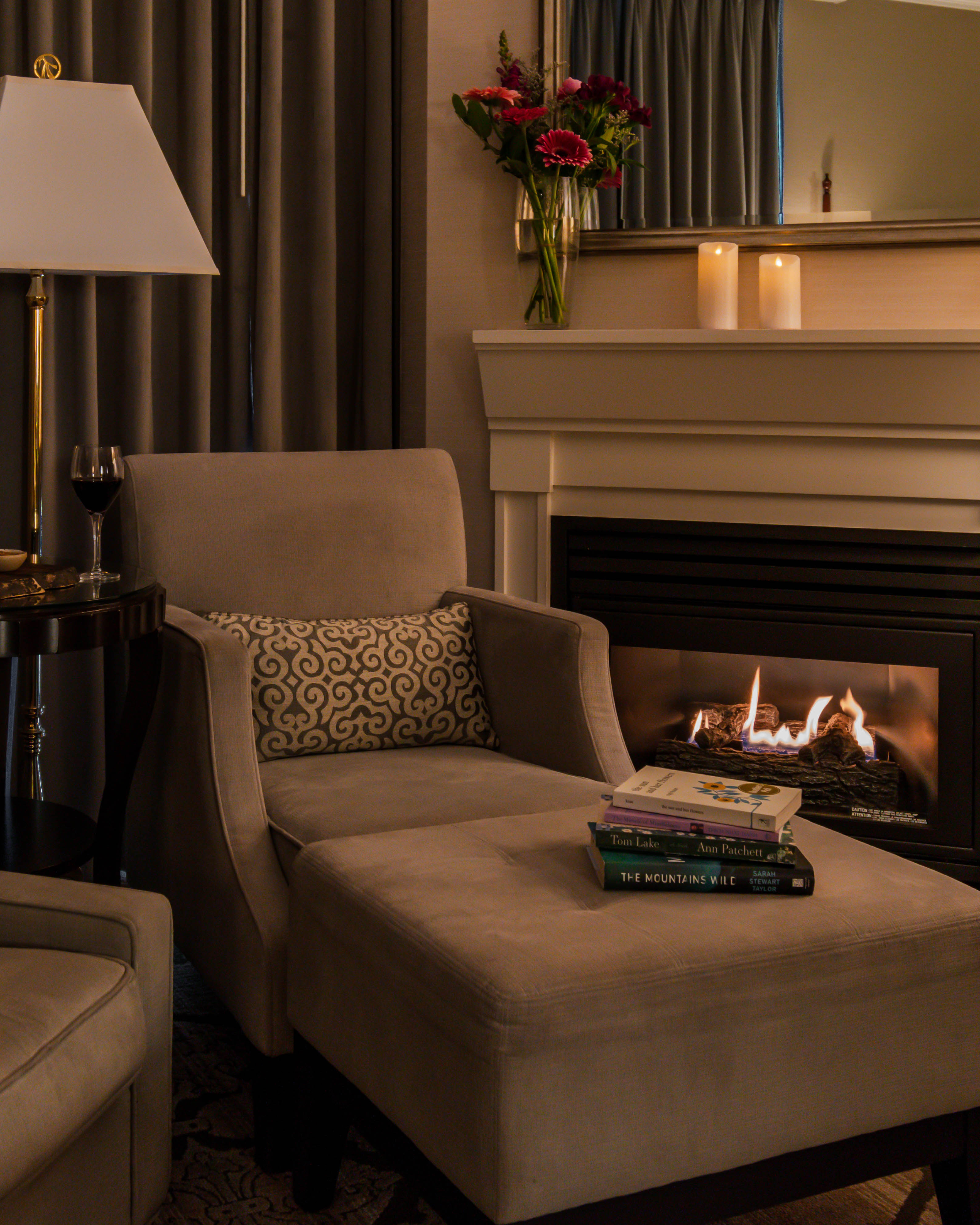 A bottle of champagne with 2 glasses in front of a lit fire