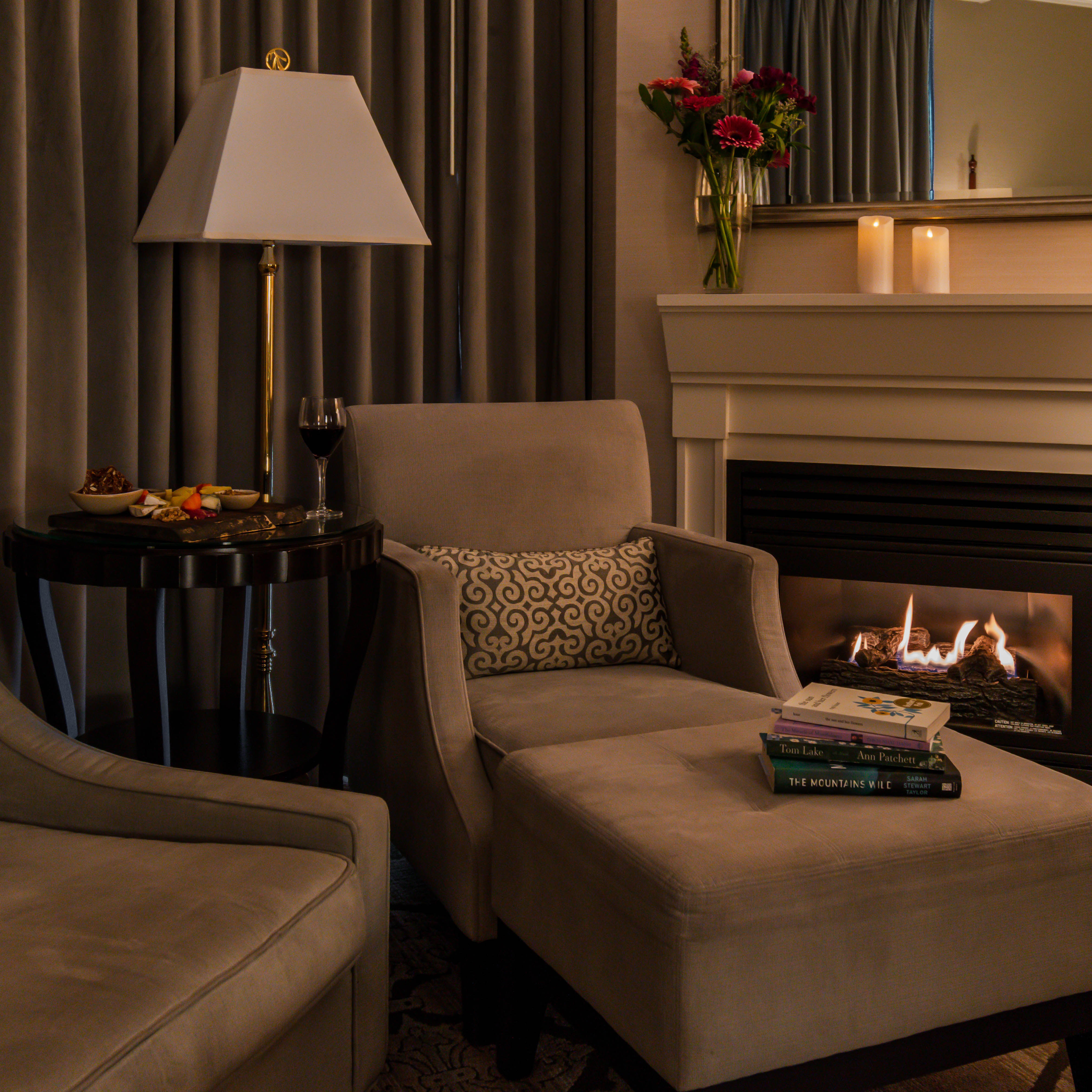 Romantic and cozy hotel room with wine, charcuterie, books and a lit fireplace 
